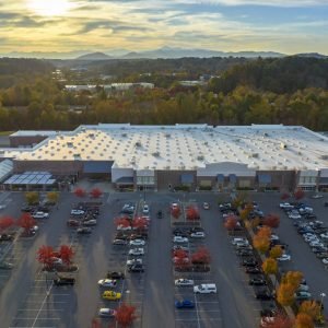 Aerial view grocery shopping mall and many colorful cars parked on parking lot with lines and markings for parking places and directions. Place for vehicles in front of a strip mall plaza.