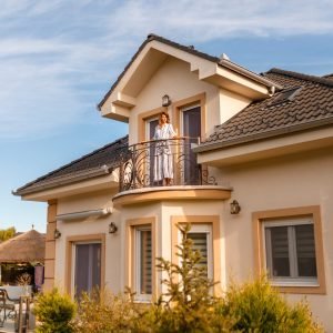 Beautiful young woman standing on her new house balcony happy after purchasing new property