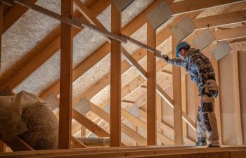 Caucasian Construction Contractor Worker in His 30s Checking on Wooden Attic and Roof Structure. Industrial Theme
